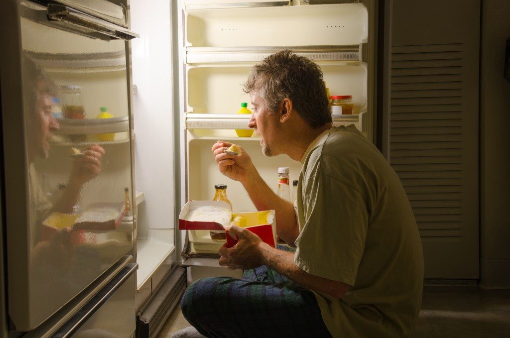 Depressed man eating in front of the fridge