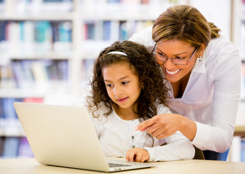a little girl in a library with mother using a laptop