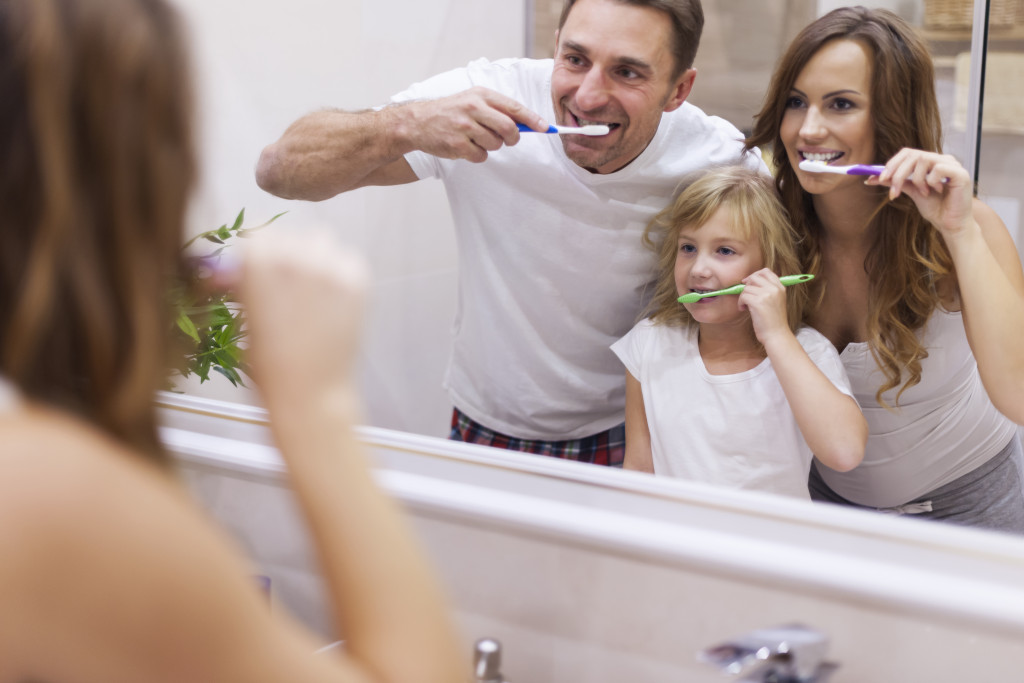 a man and a woman in the bathroom with their toddler brushing teeth together
