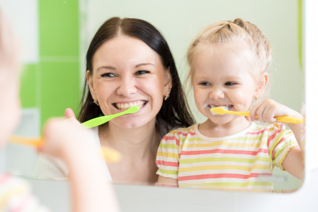 a young girl and mother brushing teeth in front of the mirror