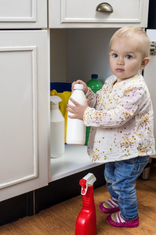 A child holding unmarked bottles of chemicals in front of an open cupboard