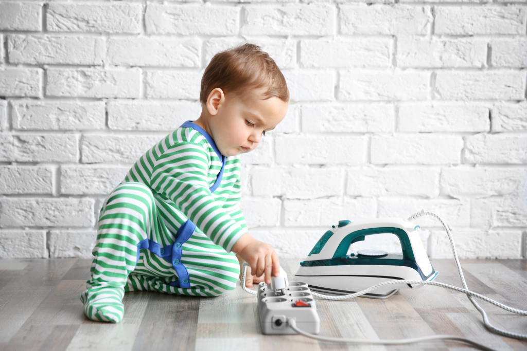 A toddler taking the plug of a steam iron out of a power extension