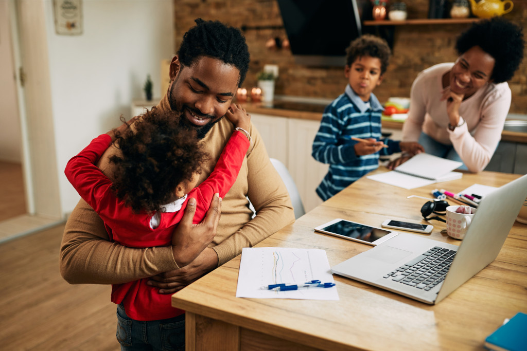 father hugging small daughter while working on computer