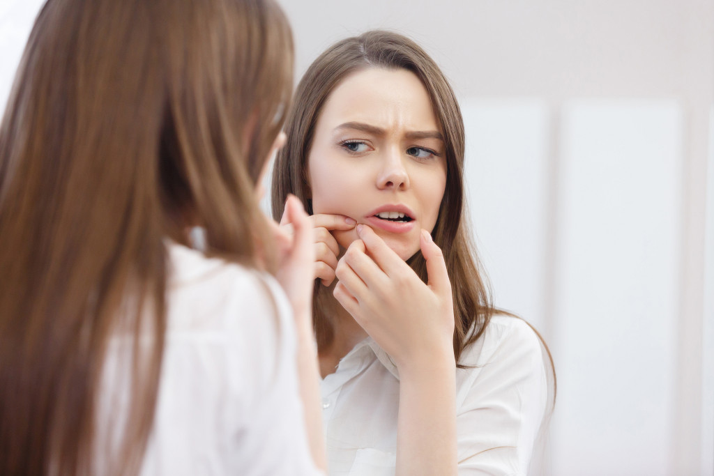 A woman looking at an acne on her face in the mirror