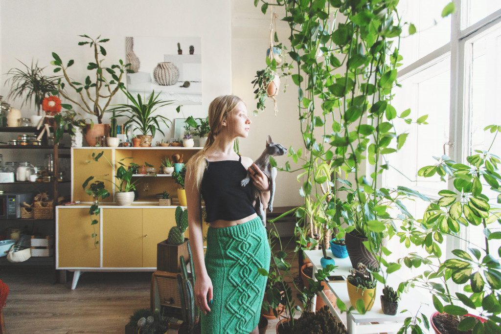 A woman holding a cat in a room full of plants