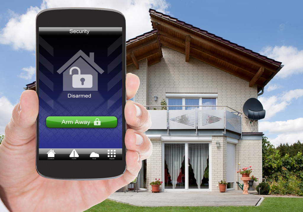 a hand holding a phone showing home security in front of a house