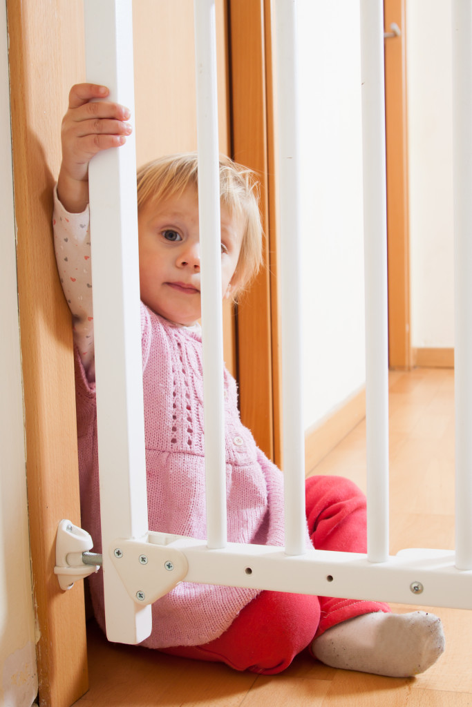 A baby sitting beside a baby gate