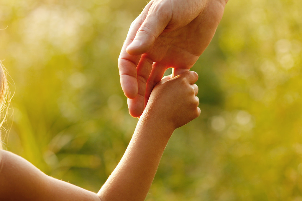 A child holding the hand of a parent outdoors