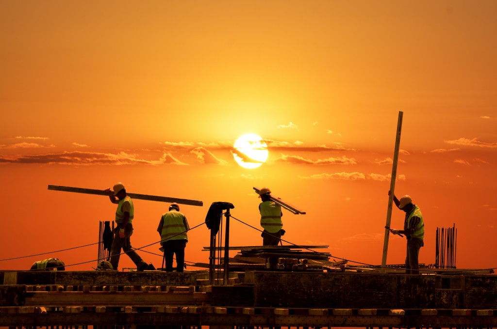 workers carrying slabs of metal in scaffoldings in sunset