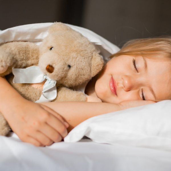 Little girl sleeping while hugging a teddy bear in her bed.