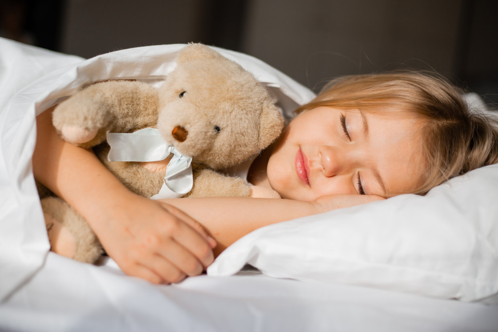 Little girl sleeping while hugging a teddy bear in her bed.