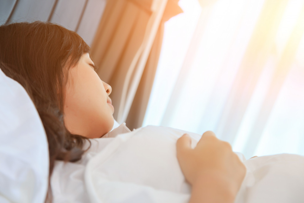 woman sleeping in a white bed with sun peeking through the curtains