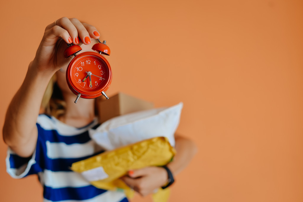 A woman holding a red alarm clock with parcels on her other hand