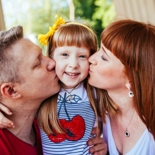 Parents kissing their daughter on each cheek