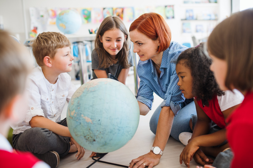 Kids in a classroom with their teacher surrounding a globe